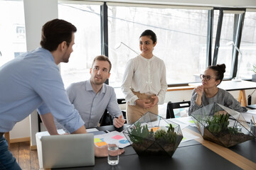 Motivated young diverse mixed race business people discussing project issues at group meeting in modern boardroom, analyzing marketing research reports or brainstorming ideas together in office.