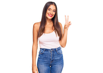 Young hispanic woman wearing casual clothes smiling with happy face winking at the camera doing victory sign. number two.