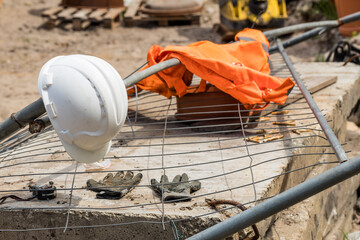 construction helmet and reflective vest lying on a knocked down metal mesh and concrete slab, in the background a construction site
