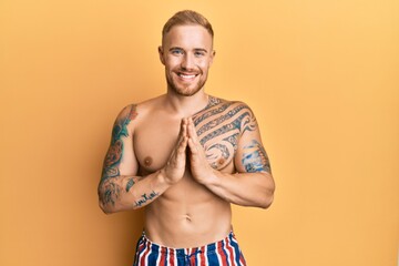 Fototapeta premium Young caucasian man wearing swimwear shirtless praying with hands together asking for forgiveness smiling confident.