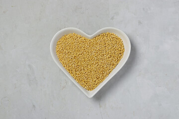 Raw pasta ptitim on heart-shaped plate on gray table. Top view. Horizontal format