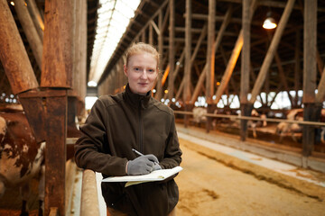Waist up portrait of young female worker holding clipboard and smiling at camera while inspecting...