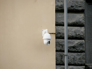 A white street surveillance camera hangs on the wall outside