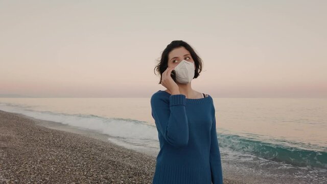 Ragazza con mascherina parla al telefono in spiaggia vicino al mare