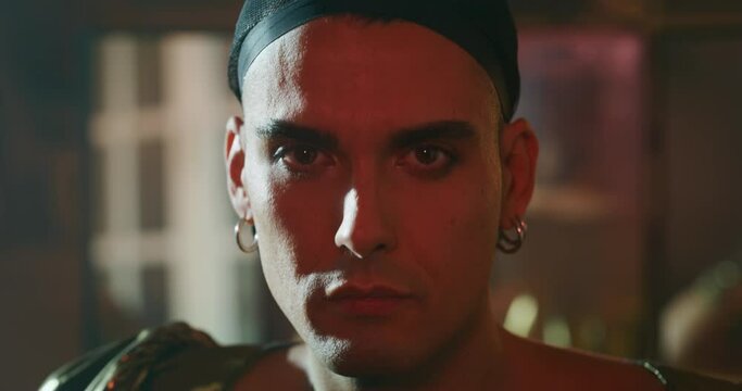 Cinematic close up shot of an young carefree homosexual male gay wearing wig cap is looking in camera while preparing in vanity room. Concept of gender expression, identity and diversity.