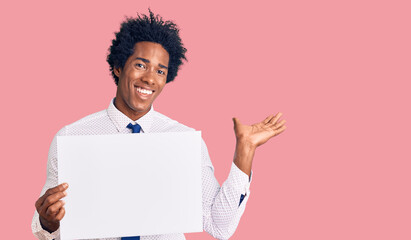 Handsome african american man with afro hair holding blank empty banner celebrating victory with happy smile and winner expression with raised hands