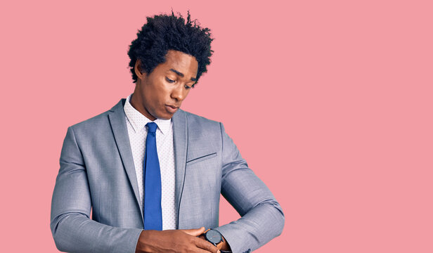 Handsome african american man with afro hair wearing business jacket checking the time on wrist watch, relaxed and confident