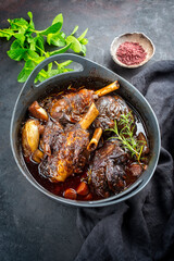 Modern style traditional braised slow cooked lamb shank in red wine sauce with shallots and carrots offered as top view in a design stewpot