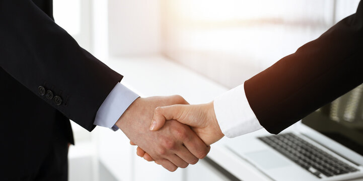 Businessman and woman shaking hands in sunny office, close-up. Concept of handshake as success symbol in business