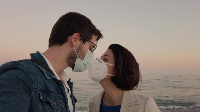 Ragazzo e ragazza si baciano con la mascherina in spiaggia di fronte al mare nel giorno di san valentino