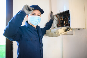 Fototapeta na wymiar Smiling technician repairing an hot-water heater wearing a mask, coronavirus concept