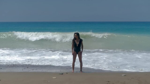Attractive Female in Swimsuit Standing on Sandy Beach, Rough Sea Waves in Back. Full Frame