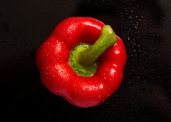 Red bell pepper on a black background. Red bell pepper in drops of water close-up.