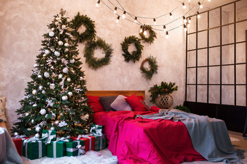 Interior of modern studio living room with comfortable bed decorated with Christmas tree and gifts