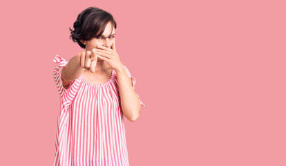 Beautiful young woman with short hair wearing casual summer clothes laughing at you, pointing finger to the camera with hand over mouth, shame expression