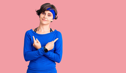 Beautiful young woman with short hair wearing training workout clothes pointing to both sides with fingers, different direction disagree