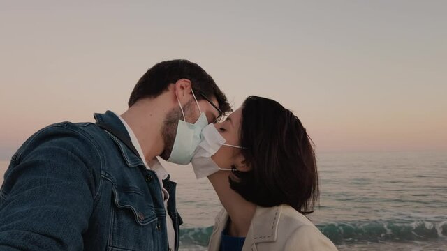 Ragazzo e ragazza si baciano con la mascherina in spiaggia a San Valentino
