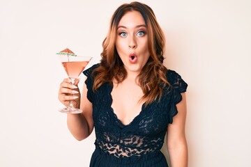 Young beautiful caucasian woman drinking tropical cocktail with alcohol scared and amazed with open mouth for surprise, disbelief face