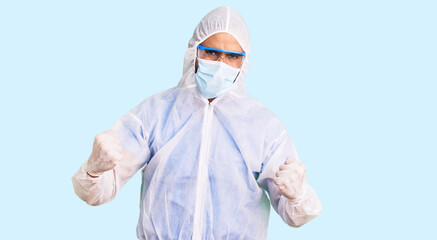 Young hispanic man wearing doctor protection coronavirus uniform and medical mask very happy and excited doing winner gesture with arms raised, smiling and screaming for success. celebration concept.