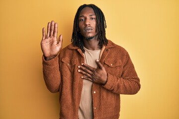 African american man with braids wearing brown retro jacket swearing with hand on chest and open...