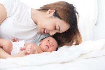 Obraz na płótnie Canvas Beautiful asian women mother long hair in the white pajamas. mom kiss at newborn infant with love, while a baby sleeping in her arm with warm, safe, comforted resting on the clean bed.