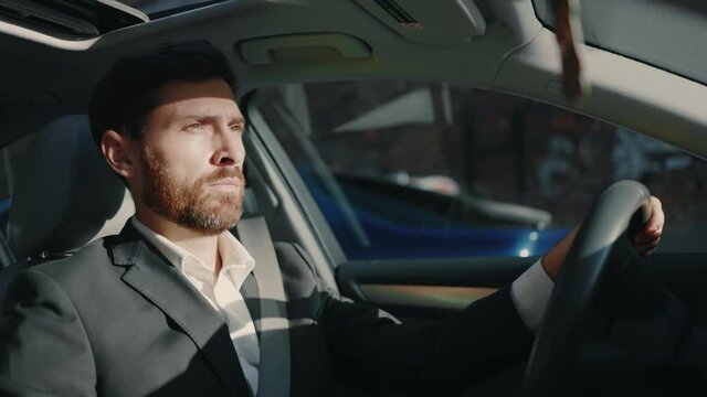 Concentrated Young Bearded Businessman Driving His Car Through Modern City In Sunlight. Entrepreneur Commuting To Work. Concept Of Business Trip, Travel, Destination.