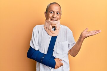 Handsome mature senior man wearing cervical collar and arm on sling smiling cheerful presenting and...