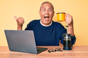 Senior handsome man with gray hair working at the office drinking a cup of coffee pointing thumb up to the side smiling happy with open mouth