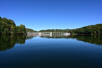 Fototapeta na wymiar Santeetlah Dam on Lake Santeetlah and Cheoah River in Graham County, North Carolina reflected in calm water of lake on clear autumn afternoon.