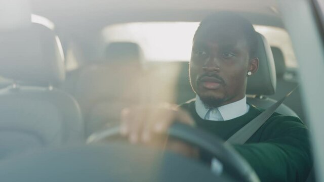 Young attractive african businessman driving car at sunsets. Concentrated careful positive guy commuting to office traveling inh city center. Business roadtrip.