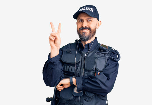 Young handsome man wearing police uniform smiling with happy face winking at the camera doing victory sign with fingers. number two.