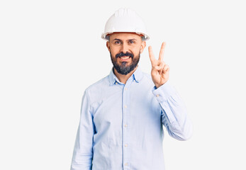 Young handsome man wearing architect hardhat showing and pointing up with fingers number two while smiling confident and happy.