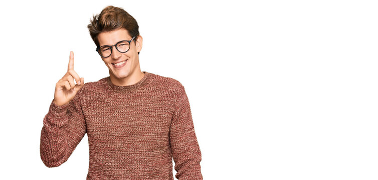 Handsome caucasian man wearing casual sweater and glasses pointing finger up with successful idea. exited and happy. number one.