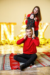 A happy family in red sweaters is sitting together on the floor. Christmas holiday atmosphere. A child in a santa costume. Family relationship concept