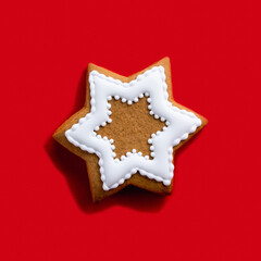 Homemade cookie. Creative bakery food. Holiday dessert adornment. Gingerbread star shape biscuit with white icing decor isolated on red background.