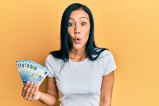Beautiful hispanic woman holding 20 euros banknotes scared and amazed with open mouth for surprise, disbelief face