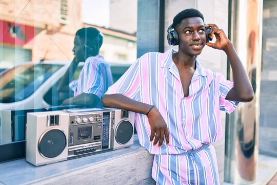 Young african american man listening to music using boom box and headphones leaning on the wall.