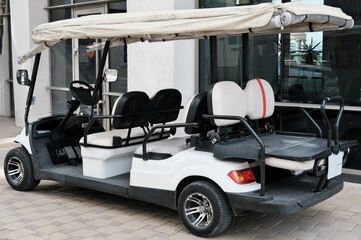 Electric buggy near hotel building. White golf cart with back seats waiting for passengers.