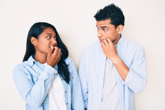 Beautiful latin young couple wearing casual clothes looking stressed and nervous with hands on mouth biting nails. anxiety problem.