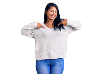 Hispanic woman with long hair wearing casual clothes looking confident with smile on face, pointing...