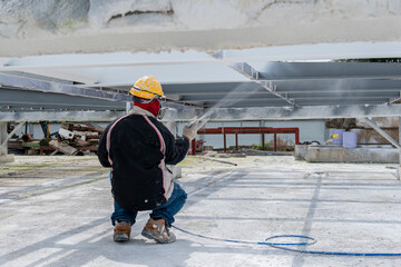 The painter is working to fireproof paint on steel structure with spray gun, at industrial factory.