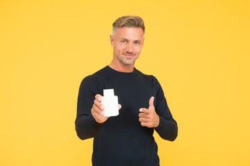 Product publicity. Happy man hold perfume pointing gun hand gesture yellow background. Skin care...