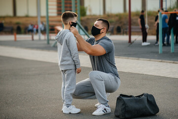 Fototapeta premium A father puts a mask on his son on the Playground after training during sunset