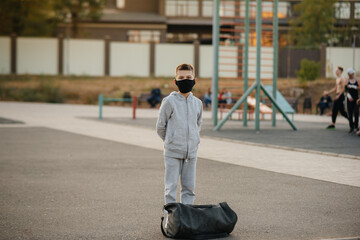 A boy stands on a sports field after an outdoor workout during sunset wearing a mask. Healthy lifestyle during the pandemic