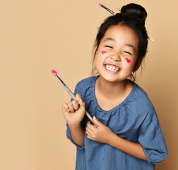 Portrait of laughing happy brunette chinese girl with painted red hearts on cheeks with brush in hair and hand
