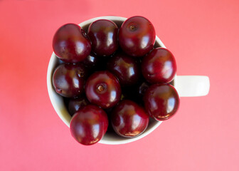 red juicy cherry in a white Cup on a red background top view . ripe summer berries