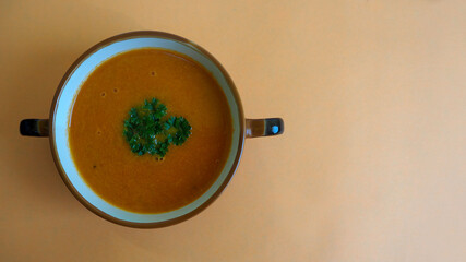 tomato soup puree with a sprig of green parsley on an orange background top view