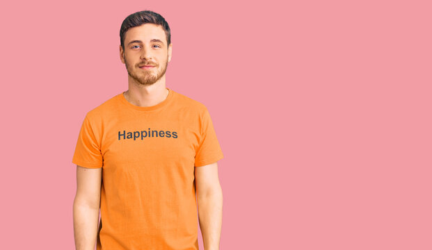 Handsome young man with bear wearing tshirt with happiness word message relaxed with serious expression on face. simple and natural looking at the camera.
