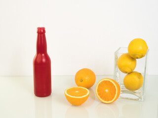 fresh yellow oranges and lemons in a glass vase on a white background, a red bottle standing next to it