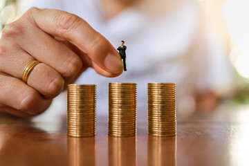 Business and Recruitment Concept. Closeup of man hand holding businessman miniature figure and put down to top of stack of gold coins.